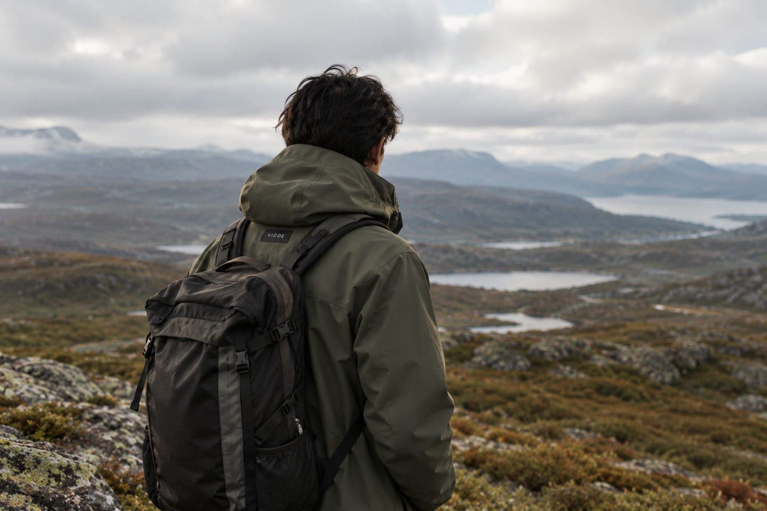 A person in a moss-green Vidde shell jacket on an open Nordic plateau