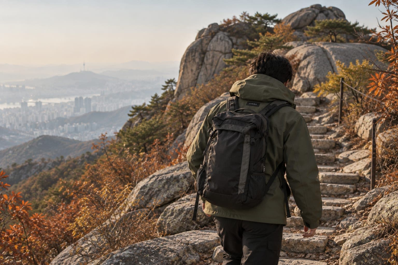 A hiker in a Vidde jacket climbing stone steps on a mountain above Seoul